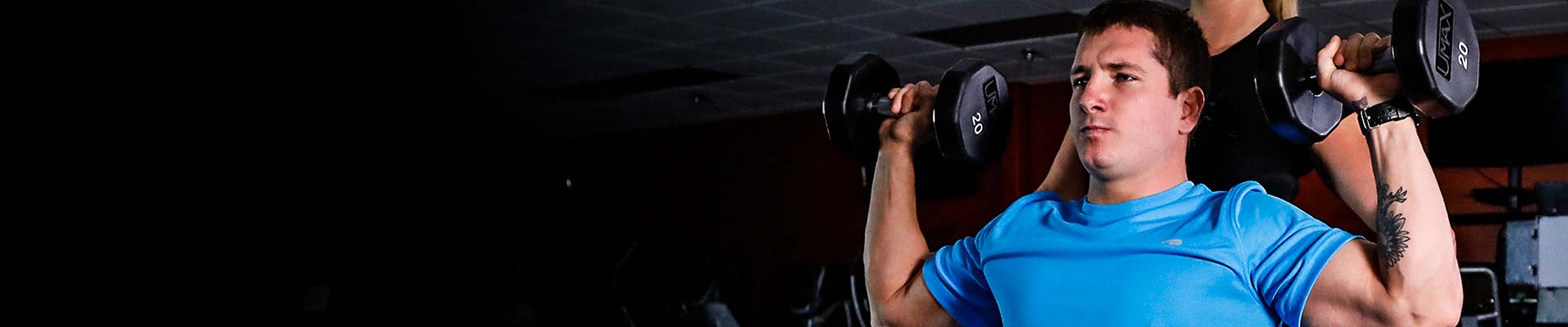 Man lifting dumbbells with personal trainer spotting behind him.