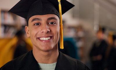 Young man smiles at the camera while wearing a graduation cap and gown