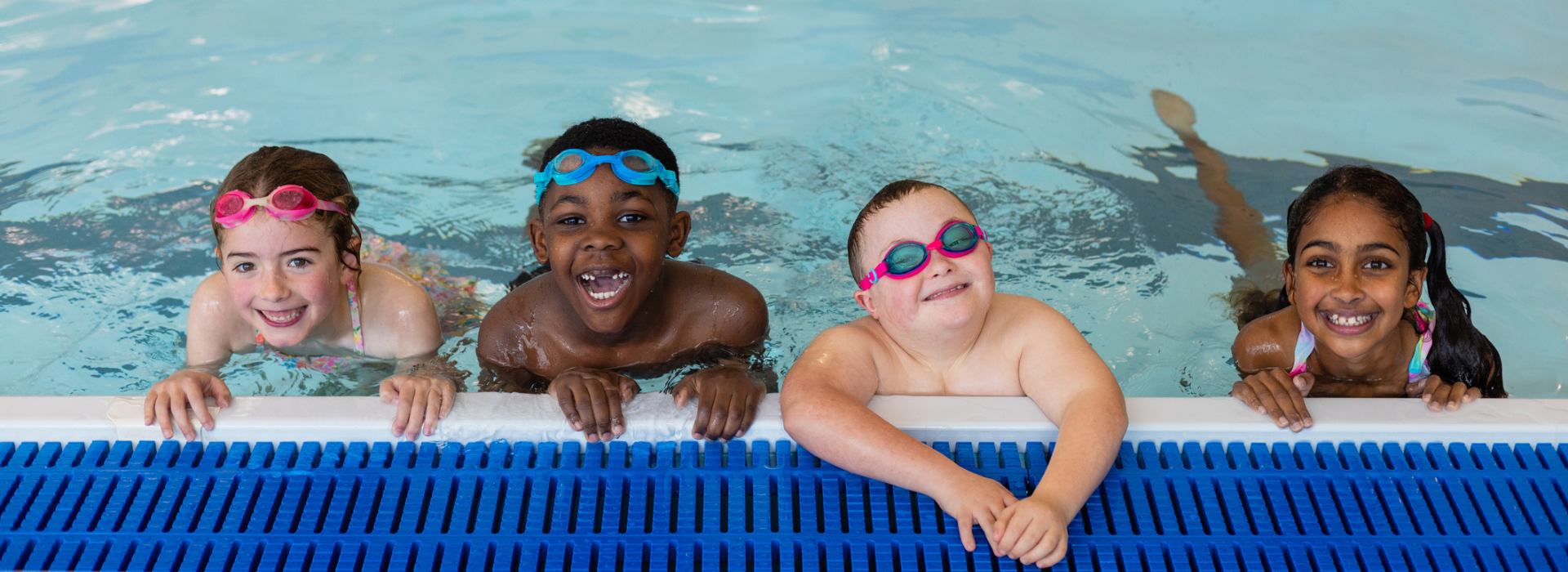 kids at the edge of a pool at swim lessons smiling