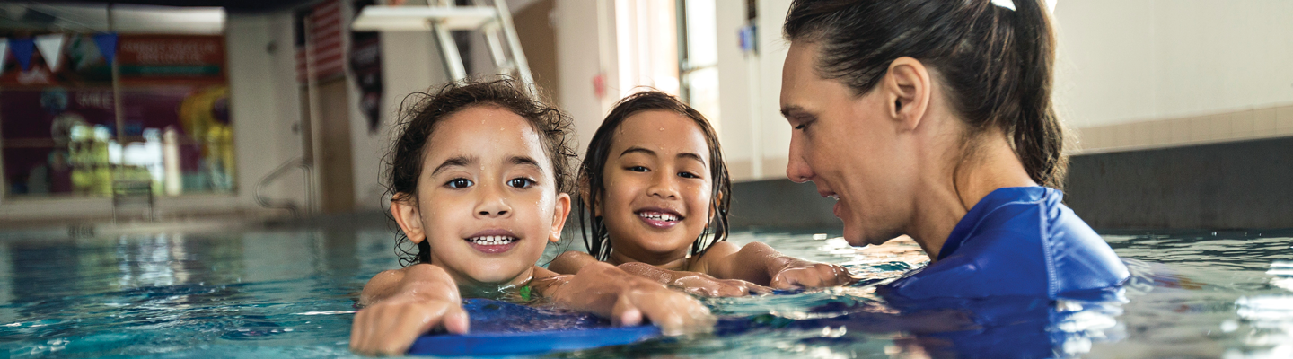 Two girls smile with YMCA swim instructor in the pool