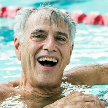 Older white male swimmer smiles at the camera at the end of the swimming pool