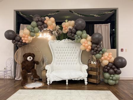 Baby shower with a large white chair, giant teddy bear, and balloon arch