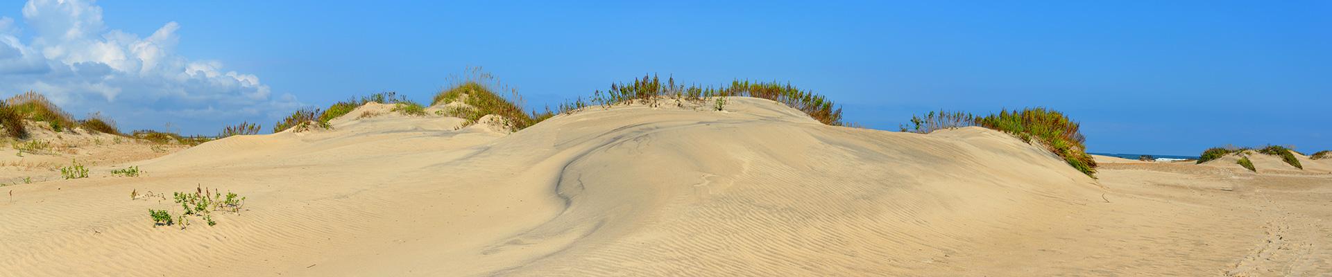 A photo of the sand dune in the Outer Banks of North Carolina near the YMCA with blue sky above