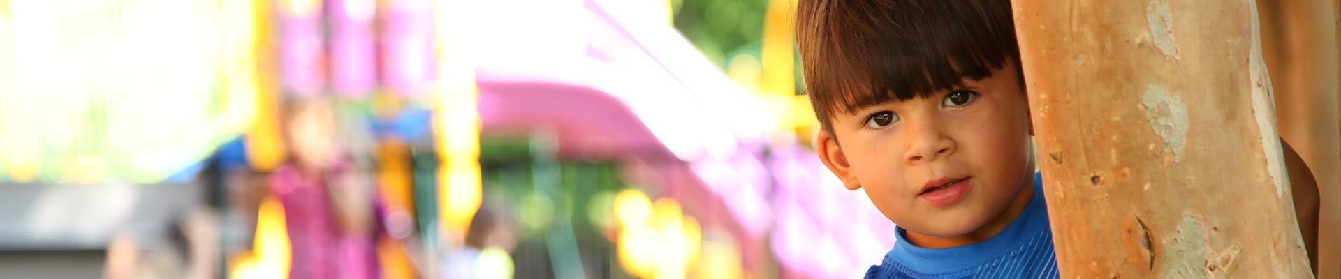 Child on playground looking out from behind a tree