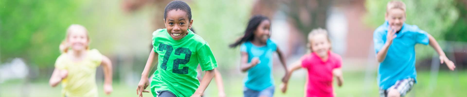 Multicultural group of kids running across the field toward the camera, smiling and laughing