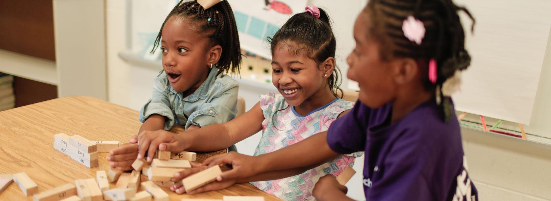 YMCA girls laughing in surprise as Jenga tower falls