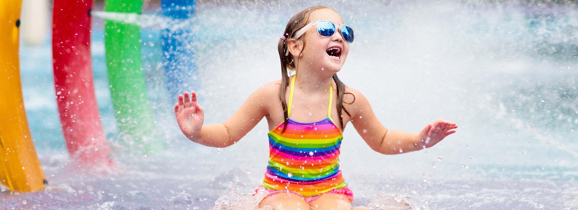 Girl laughs sitting on splash pad under water rings